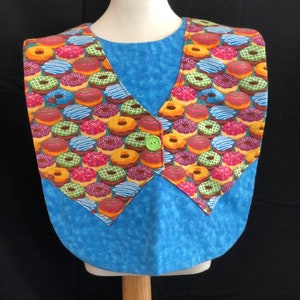 May include: A blue and yellow donut-patterned bib with a green button. The bib is on a white mannequin.