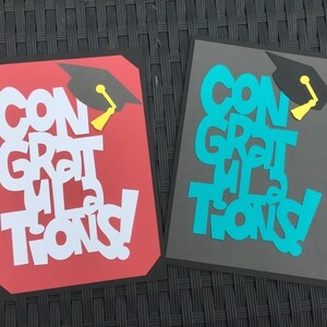 May include: Two graduation cards with the words "Congratulations" in white and turquoise letters on red and gray backgrounds. Each card has a black graduation cap with a yellow tassel.