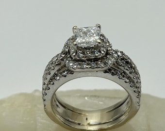 May include: A silver engagement ring set with a square-cut diamond surrounded by smaller diamonds. The band is also set with diamonds.