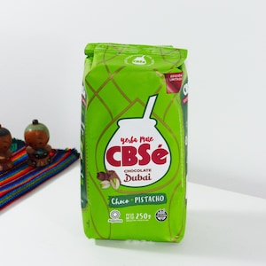 Peut inclure: Un sac vert de yerba maté CBSé au chocolat et à la pistache. Le sac présente une illustration blanche d'une gourde et d'une paille, avec du texte rouge. Le sac porte également l'inscription "Choco Pistacho" et "Dubai".