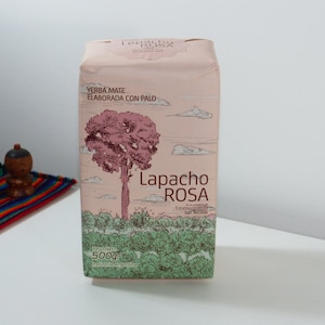 Può includere: Una scatola rosa e verde di Lapacho Rosa Yerba Mate con il testo "Yerba Mate Elaborada Con Palo" e "Lapacho ROSA" sul davanti. La scatola è da 500g ed è un prodotto argentino.