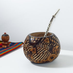 Puede incluir: Una calabaza marrón con un diseño geométrico, utilizada para beber mate, con una bombilla de plata.