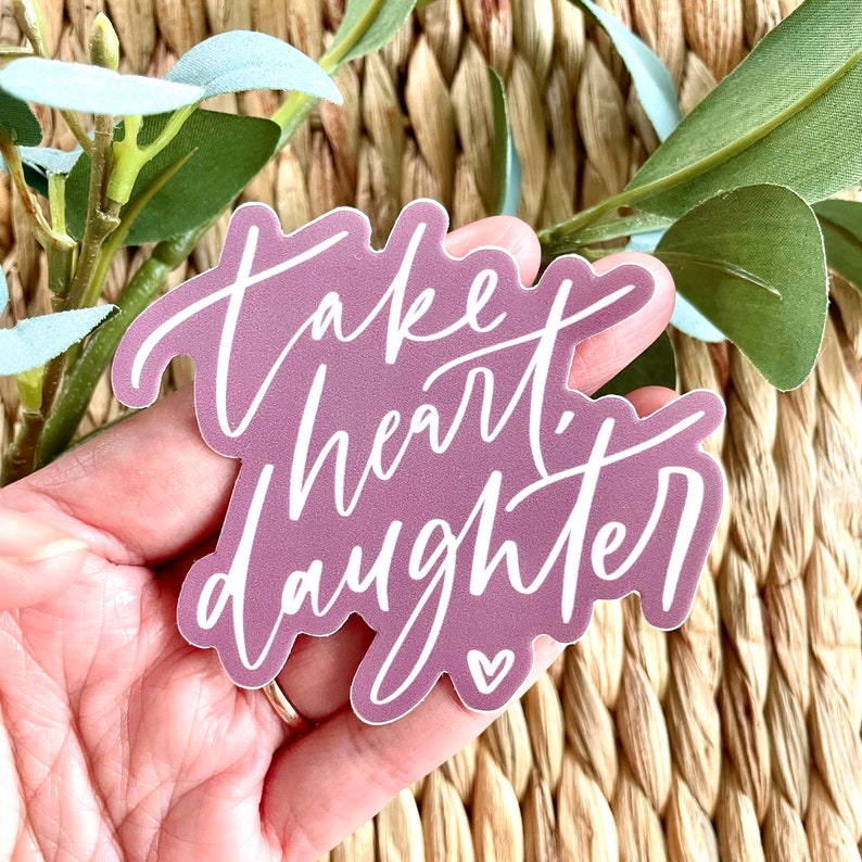 May include: A purple vinyl sticker with white lettering that reads "Take heart, daughter" with a small white heart at the bottom.