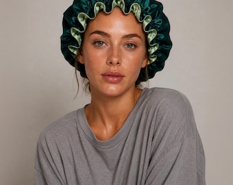 May include: A reversible satin hair bonnet featuring a deep emerald green outer layer and a contrasting light sage green inner lining. The bonnet has a gathered, ruffled edge design with a flexible elastic band for a secure fit.