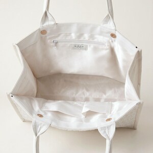 A white tote bag with a zipper and handles, open to reveal the interior.