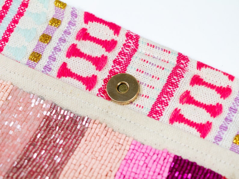 May include: A close-up of a pink and white beaded bag with a gold metal clasp. The bag has a woven fabric flap with a pink and white geometric pattern.