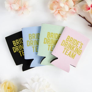 May include: Four different colored can coolers with the text "Bride's Drinking Team" in gold lettering. The coolers are black, light blue, light green, and pink.