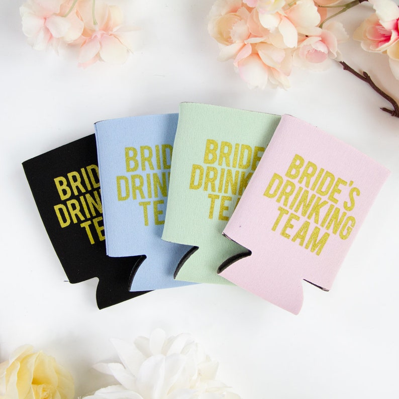 May include: Four different colored can coolers with the text "Bride's Drinking Team" in gold lettering. The coolers are black, light blue, light green, and pink.