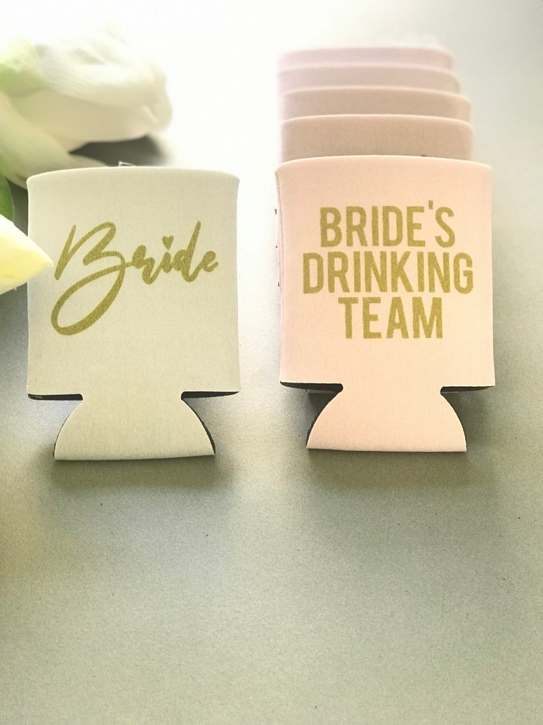 May include: Two foam beverage insulators, one white with the word "Bride" in gold lettering and one pink with the text "Bride's Drinking Team" in gold lettering.