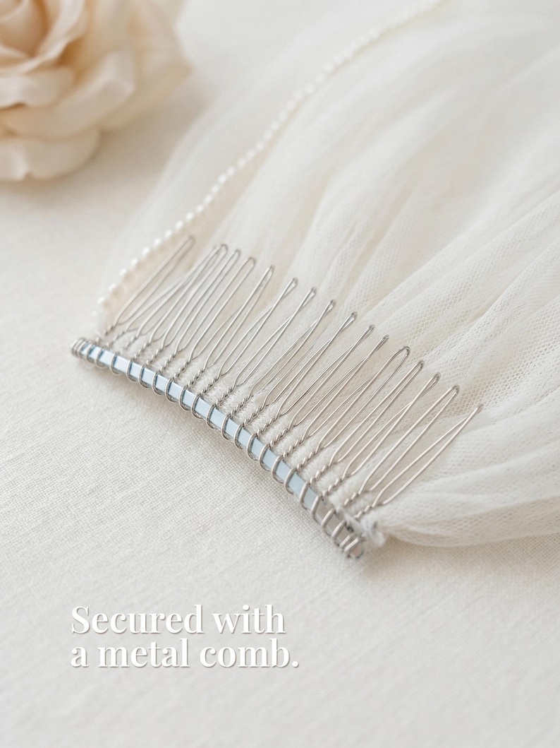 A silver metal comb rests on a white fabric, secured with a pearl bead.