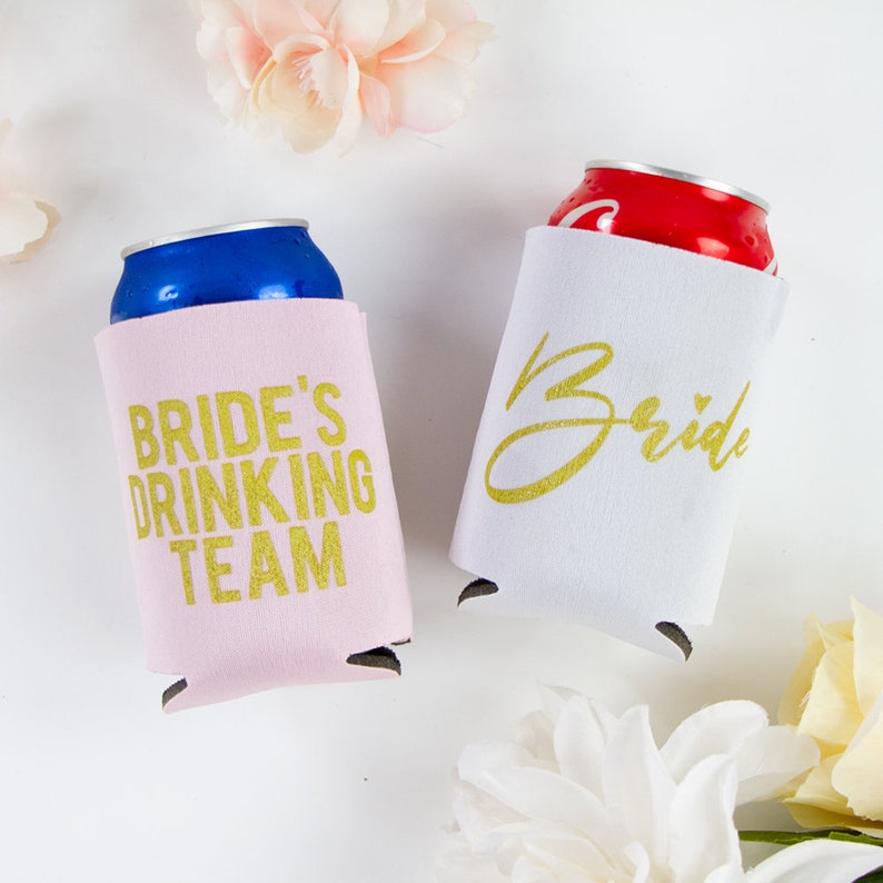 May include: Two pink and white can coolers with gold lettering. One cooler says "Bride's Drinking Team" and the other says "Bride".