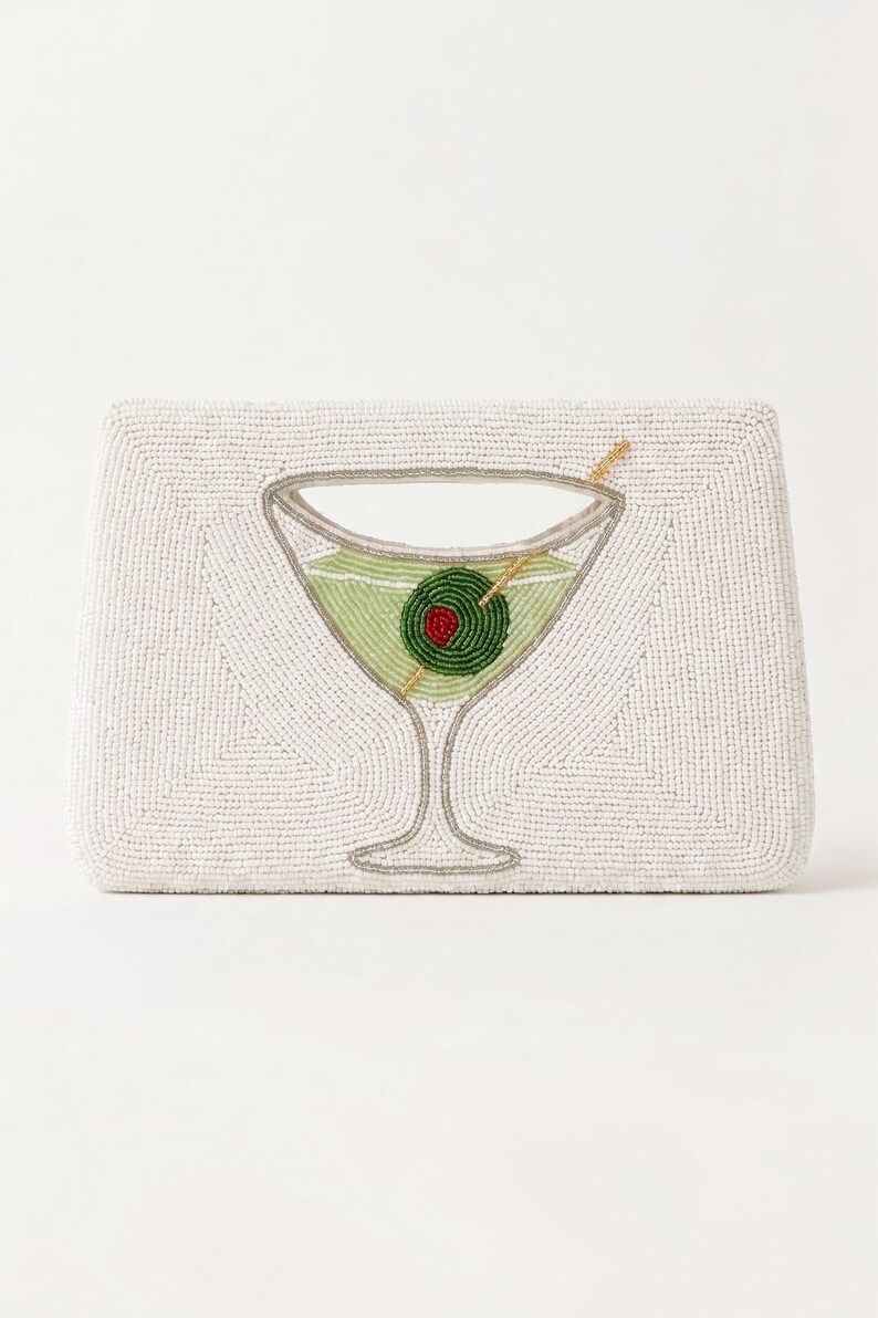 K&ouml;nnte beinhalten: Wei&szlig;es Perlen-Etui mit Martini-Glas-Design. Das Glas ist mit gr&uuml;ner Fl&uuml;ssigkeit und einer rot-zentrierten Olive gef&uuml;llt. Die Clutch hat eine rechteckige Form und einen silberfarbenen Umriss.