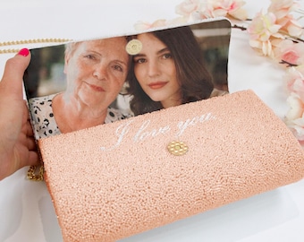 May include: A rose gold beaded clutch bag featuring a custom photo print on the interior flap showing two people. The exterior is covered in small rose gold beads with the script text I love you embroidered in white thread above a gold snap.