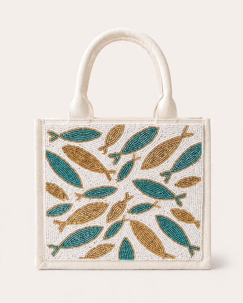 May include: Off-white tote bag with a beaded fish design. The bag features a white background with teal and gold fish patterns. The bag has a sturdy handle and a rectangular shape.