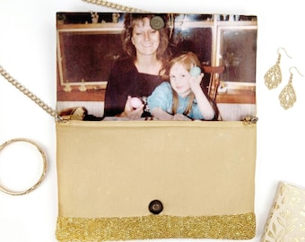 May include: A rectangular clutch bag featuring a custom photo print of an adult and child on the flap. The bag has a gold beaded bottom panel, a gold chain strap, and a magnetic snap closure. Included are gold filigree earrings and a gold bangle.