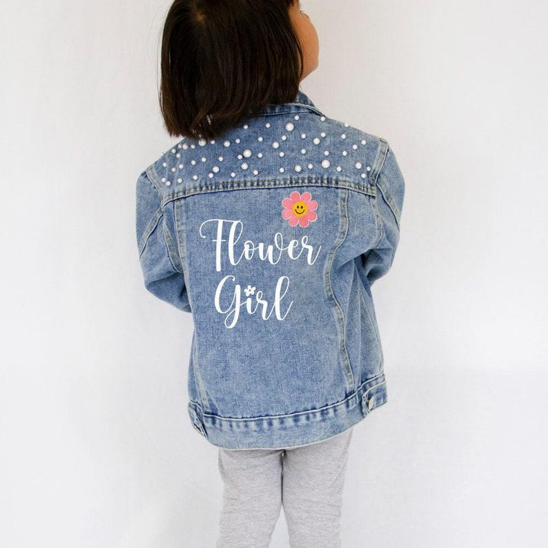 a little girl wearing a jean jacket with flowers on it