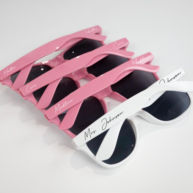 May include: Set of pink and white sunglasses with personalized names, including "Hallie", "Cara", "Madeline", and "Mrs. Johnson".