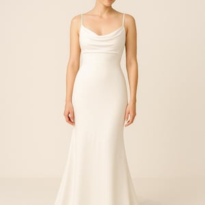 May include: A white wedding dress with a cowl neckline and spaghetti straps. The dress has a fitted bodice and a flowing, floor-length skirt. The bride's hair is styled in a low bun.