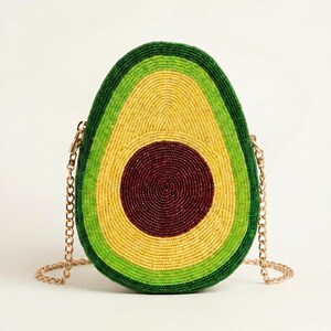 May include: A crossbody bag shaped like a halved avocado, covered in small beads. The design features a dark brown center pit, surrounded by concentric rings of light yellow, bright lime green, and a dark green outer edge, with a gold chain strap.