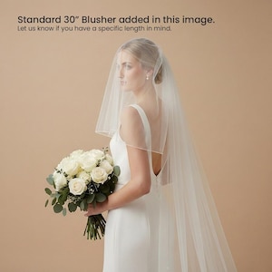 A woman in a white wedding dress holding a bouquet of white roses stands against a peach-colored background.
