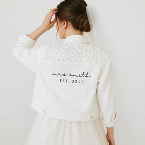Op de afbeelding: Een witte keramische mok met een zwart handvat en de tekst "But First, Coffee" in een vetgedrukte, zwarte letter. De mok staat tegen een vage achtergrond, wat een gezellige omgeving suggereert.