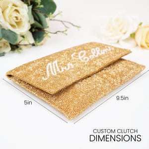 A gold clutch purse with the name "Mrs. Bollins" printed on it, along with measurements indicating it is 5 inches in length and 9.5 inches in width.