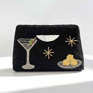 K&ouml;nnte beinhalten: Schwarze, perlenbesetzte Clutch mit Henkel, verziert mit einem Martiniglas, Sternen und einem Teller mit K&auml;sew&uuml;rfeln. Die Clutch hat eine rechteckige Form mit einer geschwungenen Griff&ouml;ffnung.