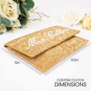 A gold clutch purse with the name "Mrs. Bollins" printed on it, along with measurements indicating it is 5 inches in length and 9.5 inches in width.