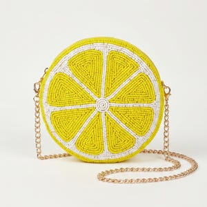May include: A round crossbody bag shaped like a lemon slice, featuring vibrant yellow and white glass beads arranged in a radial pattern. The bag includes a thin, metallic gold-tone chain strap attached to the sides with small lobster clasps.