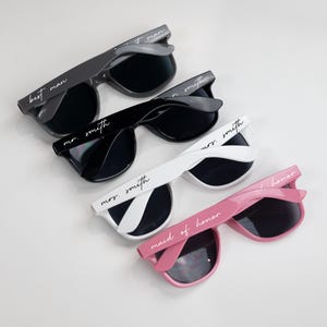 May include: Four pairs of sunglasses with different colored frames and black lenses. The sunglasses have white text on the frames that reads "best man", "mr. smith", "mrs. smith", and "maid of honor".