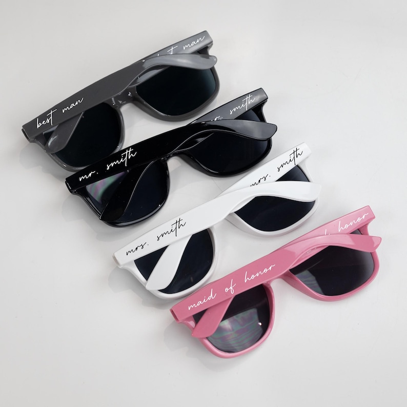 May include: Four pairs of sunglasses with different colored frames and black lenses. The sunglasses have white text on the frames that reads "best man", "mr. smith", "mrs. smith", and "maid of honor".