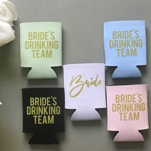 May include: Five different colored can coolers with gold lettering. The coolers say "Bride's Drinking Team" and one says "Bride".