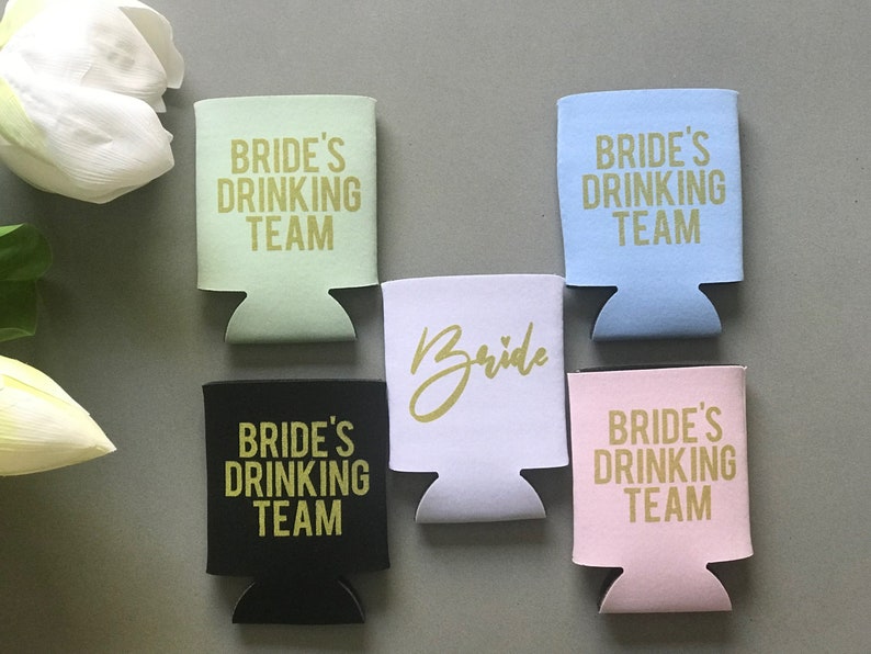 May include: Five different colored can coolers with gold lettering. The coolers say "Bride's Drinking Team" and one says "Bride".