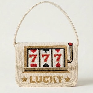 May include: A rectangular beaded handbag featuring a slot machine graphic with three red sevens and card suit symbols. The bag has a cream-colored background, a single top handle, and the word LUCKY embroidered in gold with stars on the front flap.