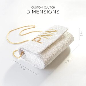 a white clutch purse with gold lettering on it.