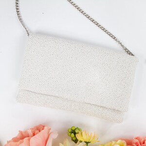 a white purse sitting on top of a table next to flowers