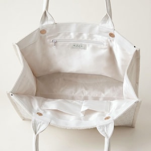A white tote bag with a zipper and handles, open to reveal the interior.
