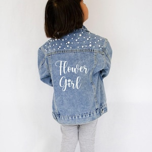 a little girl wearing a jean jacket that says flower girl