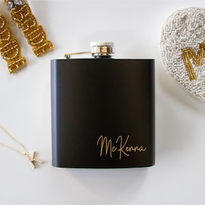 May include: Black metal flask with a silver lid and the name "McKenna" engraved in gold lettering.