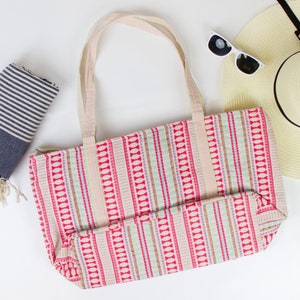 May include: A pink and white striped tote bag with a blue and white striped beach towel and a straw sun hat with a black ribbon.