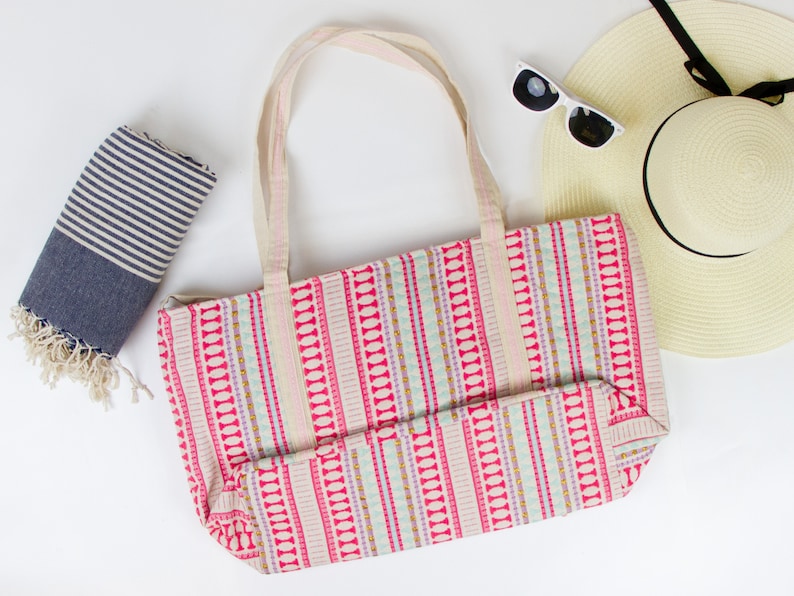 May include: A pink and white striped tote bag with a blue and white striped beach towel and a straw sun hat with a black ribbon.