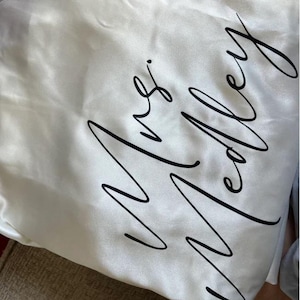 Può includere: Accappatoio di raso bianco con il testo "Mrs. Medley" scritto in corsivo nero.
