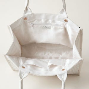A white tote bag with a zipper and handles, open to reveal the interior.