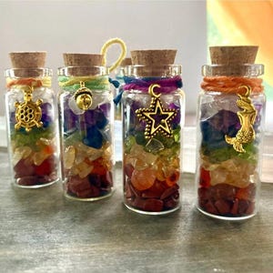 May include: Four small glass bottles filled with colorful crystals and topped with cork stoppers. Each bottle has a different charm attached to the cork, including a turtle, acorn, star, and mermaid.