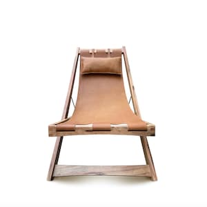 May include: A brown leather folding chair with a wooden frame. The chair has a pillow for added comfort.