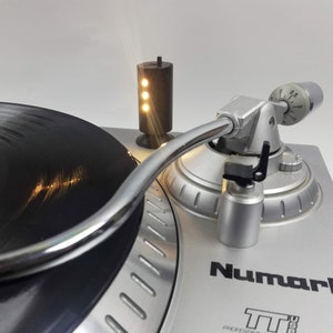 May include: A silver Numark TTUSB professional turntable with a black vinyl record. A small black light with three illuminated bulbs stands to the left. The turntable's tonearm is chrome.