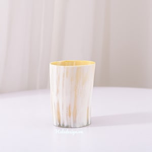 Könnte beinhalten: Eine weiße und gelbe Keramiktasse mit strukturierter Oberfläche. Die Tasse steht auf einer weißen Oberfläche.