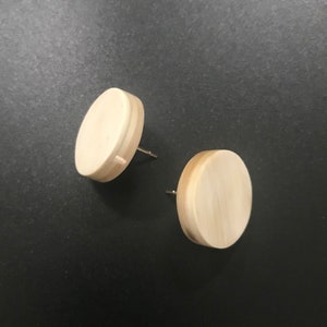 Puede incluir: Un par de pendientes redondos de madera de color marrón claro. Los pendientes son simples y de diseño minimalista.
