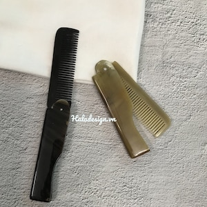 May include: Two combs, one black and one brown, are shown on a textured surface. The black comb is a folding comb with a black handle and a black comb. The brown comb is a folding comb with a brown handle and a brown comb.