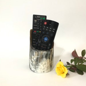 May include: A black and white horn remote control holder with two black remote controls inside. A yellow rose is on the white surface next to the holder.